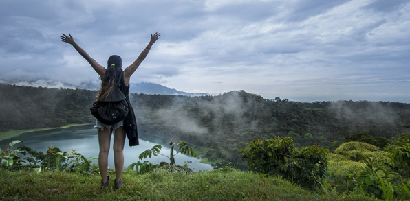 Kvinde står med løftede arme foran en kratersø i Costa Rica
