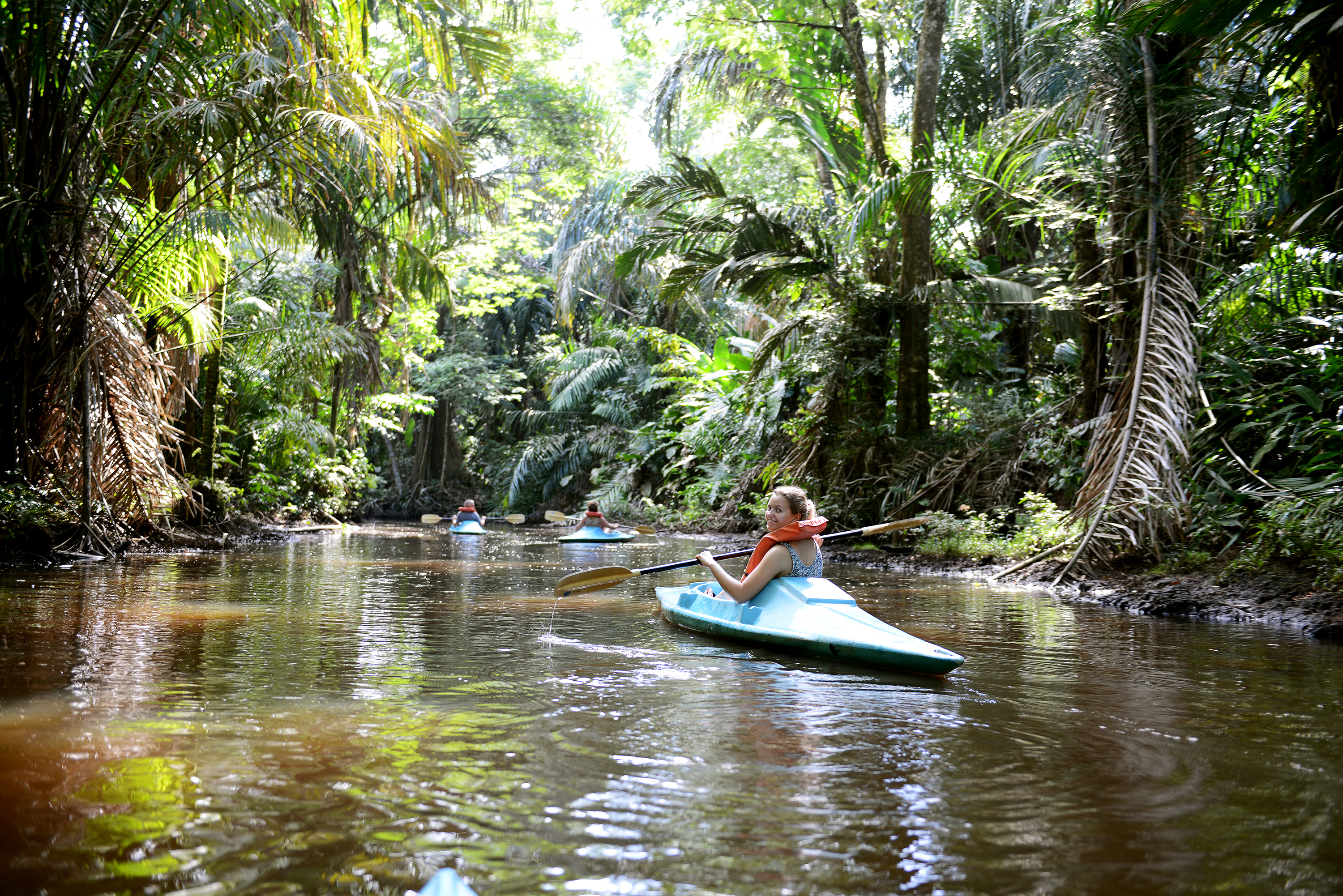 Ung kvinde padler i blå kajak gennem grøn jungle i Tortuguero i Costa Rica
