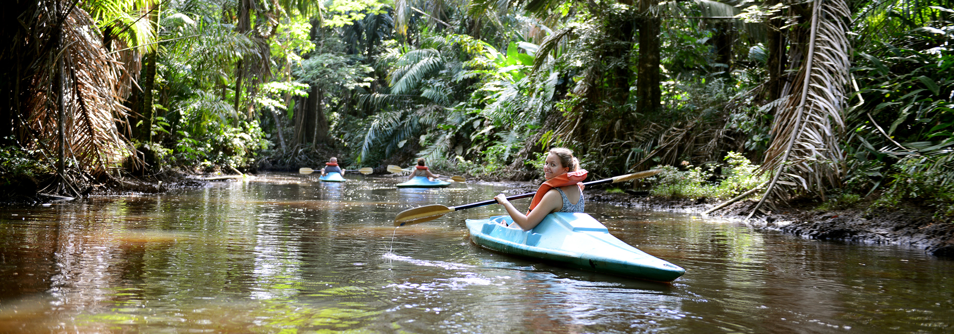 Ung kvinde padler i blå kajak gennem grøn jungle i Tortuguero i Costa Rica