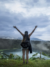 Kvinde står med løftede arme foran en kratersø i Costa Rica