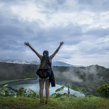 Kvinde står med løftede arme foran en kratersø i Costa Rica