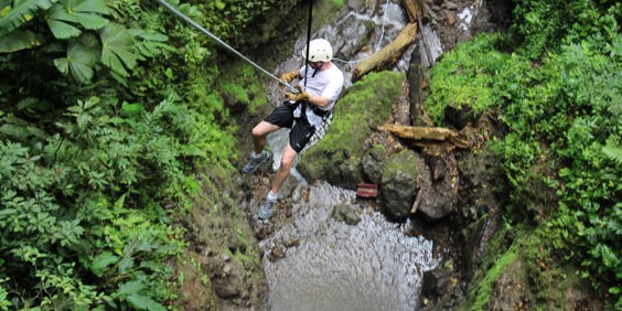Mand i shorts, t-shirt og hjelm rapeller i en frodig kløft ved Arenal i Costa Rica.