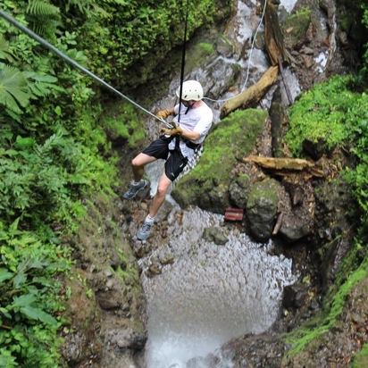 Mand i shorts, t-shirt og hjelm rapeller i en frodig kløft ved Arenal i Costa Rica.
