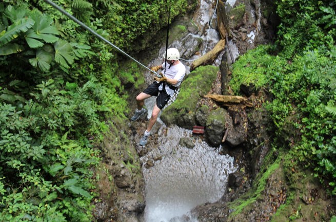 Mand i shorts, t-shirt og hjelm rapeller i en frodig kløft ved Arenal i Costa Rica.